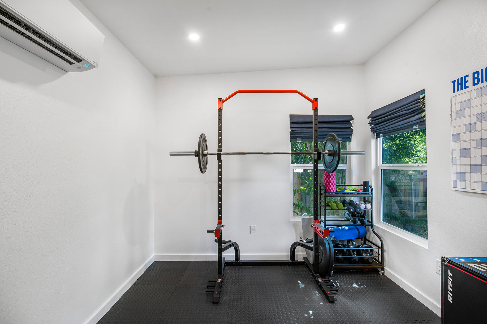 Home gym interior with power rack, barbell, and mini-split AC